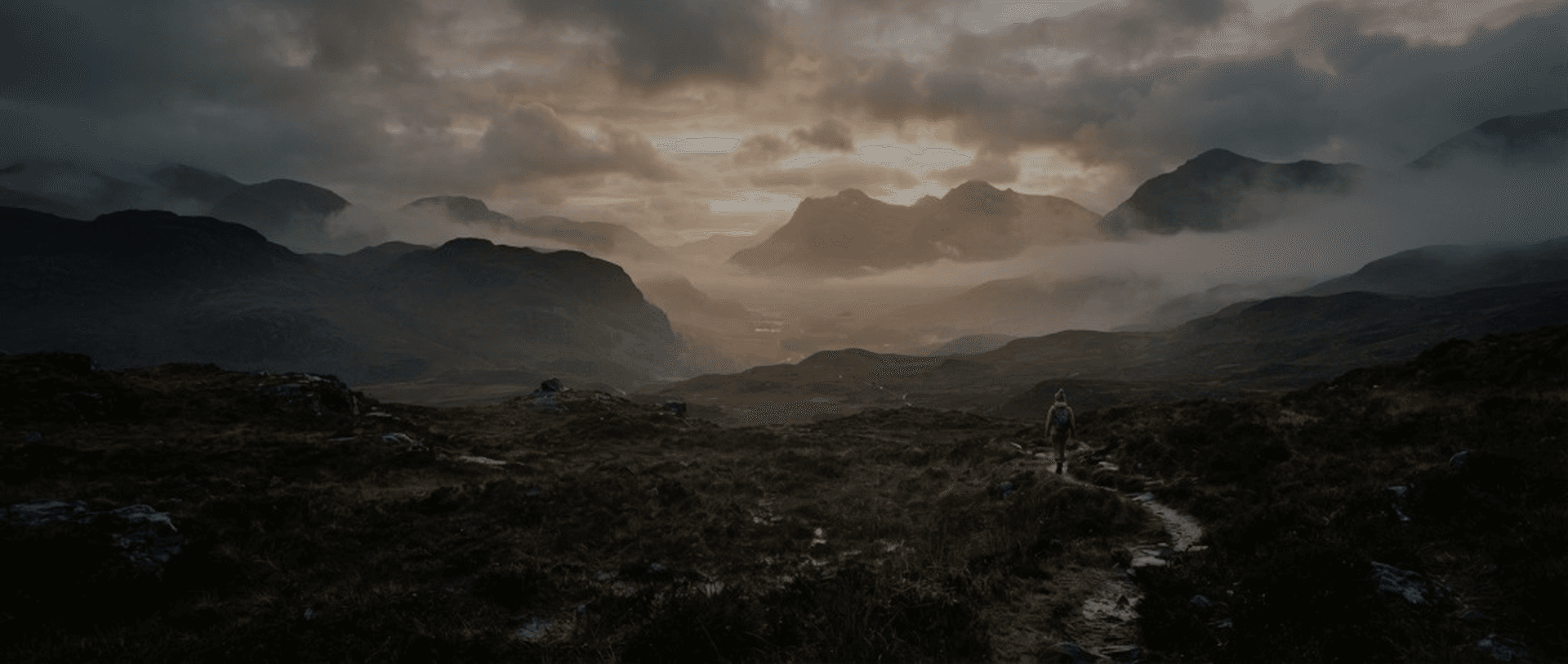 Hiker on a mountain path through a misty valley in golden light